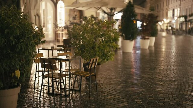 Empty coffee table and chairs in Ljubljana city at night in rain 4K
