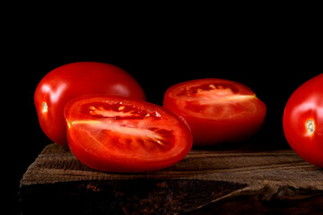 Plum tomato cut into halves on the old wooden board against the black background. Low key
