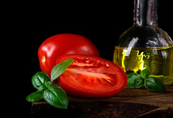 Plum tomato, olive oil and fresh basil on the old wooden board against the black background. Ingredients for cooking a salad and other meals. Low key