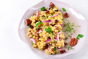 Salad with couscous, dried cranberry, pecan nuts, red onion, microgreen and orange dressing on the ceramic plate. Healthy vegan meal