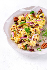 Salad with couscous, dried cranberry, pecan nuts, red onion, microgreen and orange dressing on the ceramic plate. Healthy vegan meal