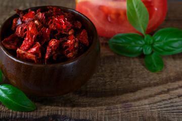 Diced dried tomato in the bowl, basil leaves and plum tomato half on the wooden board. Natural ingredient