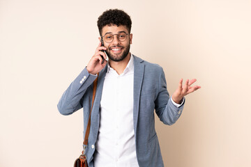 Young business Moroccan man isolated on beige background keeping a conversation with the mobile phone with someone