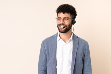 Telemarketer Moroccan man working with a headset isolated on beige background thinking an idea while looking up