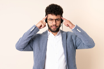 Telemarketer Moroccan man working with a headset isolated on beige background having doubts and thinking