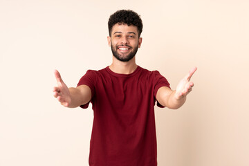 Young Moroccan man isolated on beige background presenting and inviting to come with hand