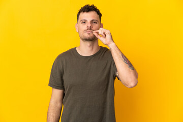 Young caucasian handsome man isolated on yellow background showing a sign of silence gesture