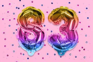 Rainbow foil balloon number, digit eighty three on a pink background with sequins. Birthday greeting card with inscription 83. Top view. Numerical digit. Celebration event, template.