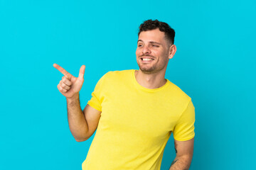 Fototapeta premium Young caucasian handsome man isolated on blue background pointing finger to the side and presenting a product
