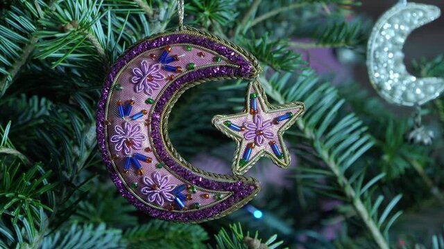 A closeup of a purple, mauve, beaded, Christmas ornament with minature moon and star gently moving while hanging in an evergreen tree