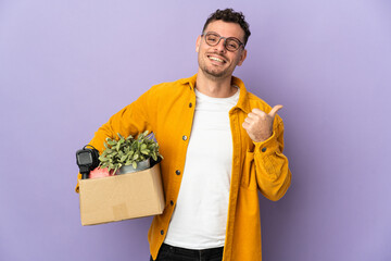 Young caucasian man making a move while picking up a box full of things isolated on purple...