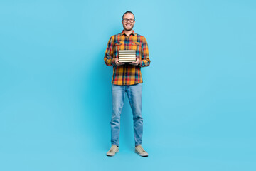 Full size photo of smart young brunette guy hold book wear checkered shirt jeans sneakers isolated on blue color background
