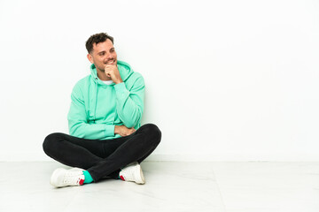 Young handsome caucasian man sitting on the floor looking to the side