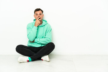 Young handsome caucasian man sitting on the floor surprised and shocked while looking right