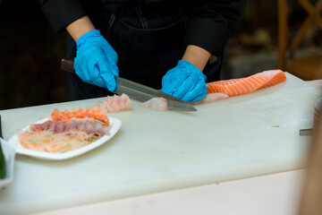 The salmon is in the hands of the experienced  chef. She is using a knife to slice salmon fillet for sashimi and sushi. A chef cutting a salmon fillet with a knife on a cutting board. Cut fish fillet 