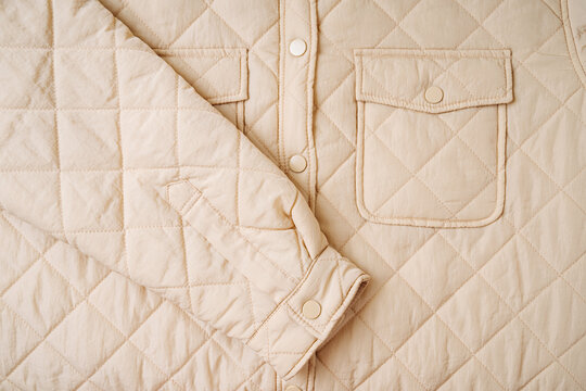 Quilted material, square quilted jacket with pocket. Beige  background texture. Close-up