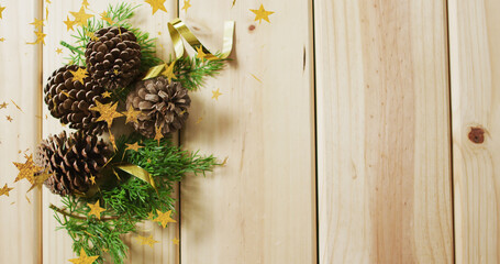 Image of stars falling over pine cones and wooden background with copy space