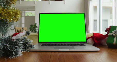 Laptop with green screen copy space on table with santa hats, christmas tree and presents