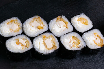 Macro shot of hosomaki sushi with soy sauce on natural black slate plate background with selective focus. Sushi with salmon and avocado