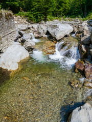 Drone photo above a mountain river forming stepped cascades and ponds when flowing through eroded large stone pieces. An old stone wall was destroyed by the water. Carpathia, Romania