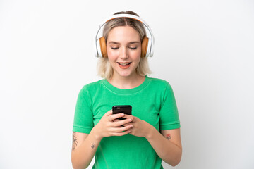 Young caucasian woman isolated on white background listening music and looking to mobile