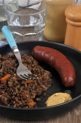Plat de lentilles avec une saucisse fumée servi dans une assiette avec de la moutarde et une fourchette à côté d'un verre d'eau