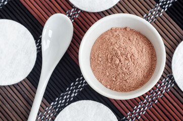 Pink bentonite clay powder in a small white bowl and cotton pads. Clay texture close up. Diy facial or hair mask, dry shampoo recipe. Natural beauty treatment and spa. Top view, copy space