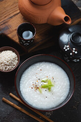 Bowl of asian congee or conjee served in a black bowl, vertical shot, high angle view