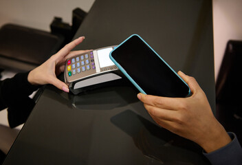 Hand of a customer holding smartphone and paying with a contactless credit card with NFC...