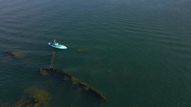 Aerial shot. Young women is having fun. Stand Up Paddling in the sea. SUP. Paddling among debrees of a sunk metal ships