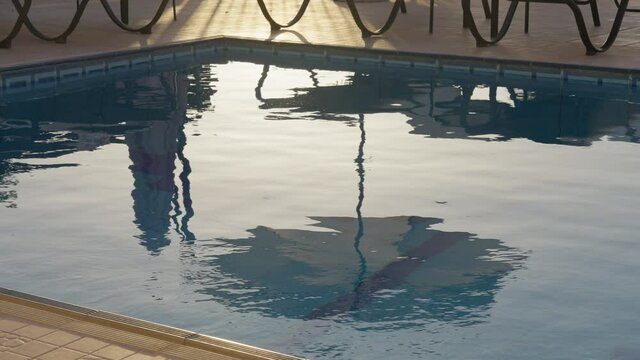 Reflection of umbrella and sun loungers in rippling swimming pool water