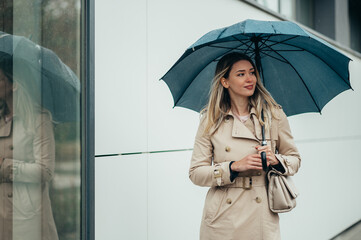 Businesswoman with umbrella walking down city street during rain