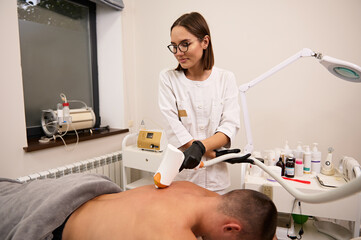 Obraz na płótnie Canvas Young man having laser hair removal procedure of back zone by specialist in cosmetic beauty spa center. Removes pigmentation in cosmetic clinic.