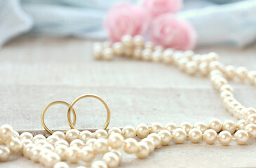 wedding rings on wooden white table, pearls beads, pink rose bouquet, selective focus