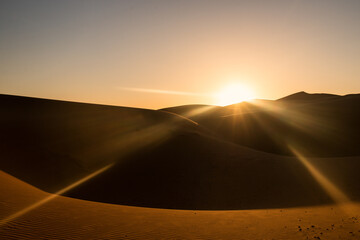 Fototapeta na wymiar The sun hides behind the red sand dunes of the Merzouga desert, Morocco