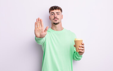 young handsome man looking serious showing open palm making stop gesture. take away coffee concept