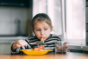 girl eating pasta with sausage in the kitchen in a striped jacket