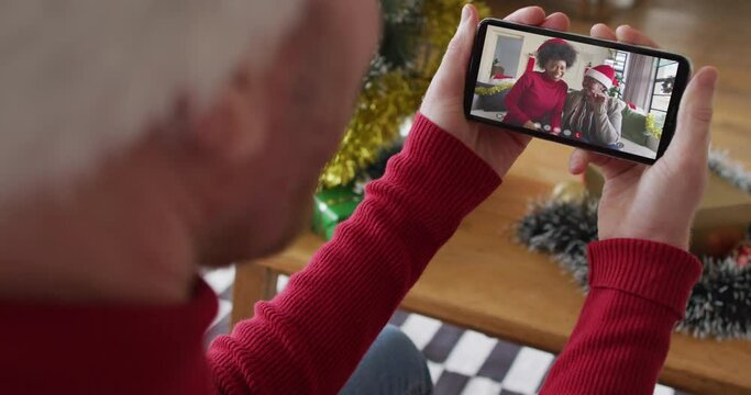 Caucasian man with santa hat using smartphone for christmas video call with smiling family on screen