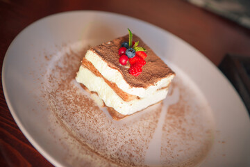 tiramisu on a white plate, sprinkled with cocoa, stands on the table