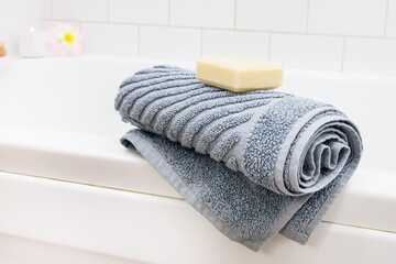 Fototapeta na wymiar Gray Towel and Soap Bar on White Bath Tub SPA and Relax at Home Horizontal