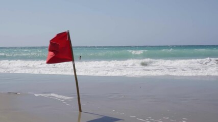 Red warning flag blowing in wind on beach with sea in background