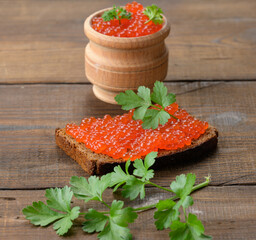 red salmon caviar lies on a piece of rye bread. Brown wooden table