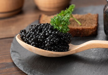 fresh grainy black paddlefish caviar in brown wooden spoon on a black background, close up
