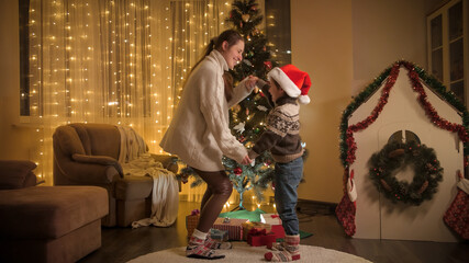 Happy cheerful mother with son dancing and having fun next to Christmas tree in living room. Pure emotions of families and children celebrating winter holidays.