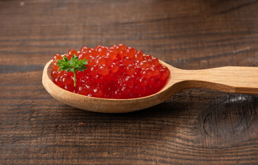 red caviar of pink salmon lies in a wooden spoon on a brown wooden table