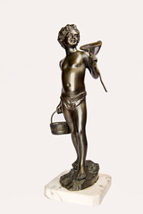 Vintage bronze figurine depicting a boy in swimwear on a rock with a crab net fishnet and basket isolated on white.