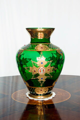 An old fine art glass flower vase with gold decorations and beads on a round wood table. Centerpiece.