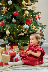 christmas, holidays and childhood concept - happy baby girl opening gifts at home