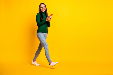 Fototapeta na wymiar Full size profile side photo of young happy cheerful positive girl go walk with phone in hands isolated on yellow color background