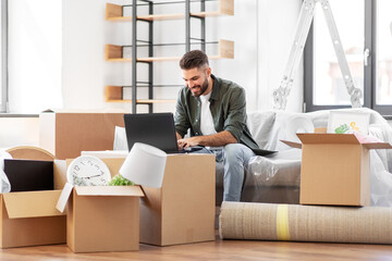 moving, people and real estate concept - happy smiling man with laptop computer at new home